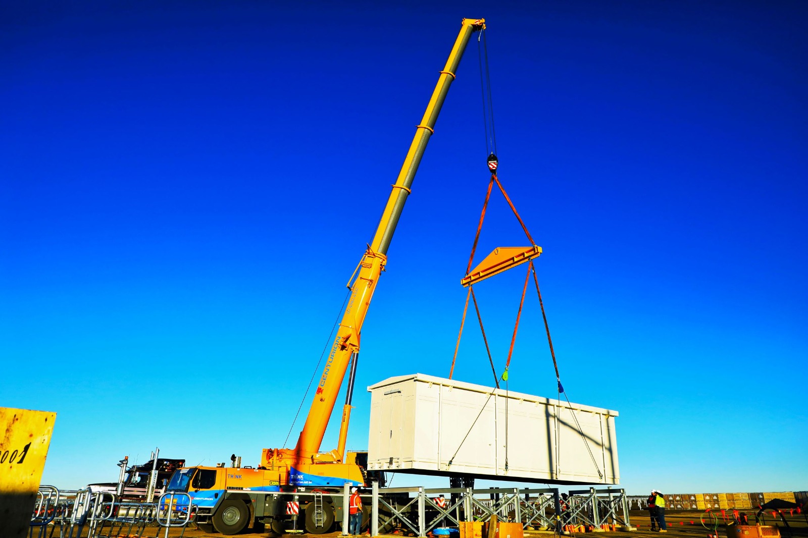 Mobile crane performing a precision lift against a clear blue sky